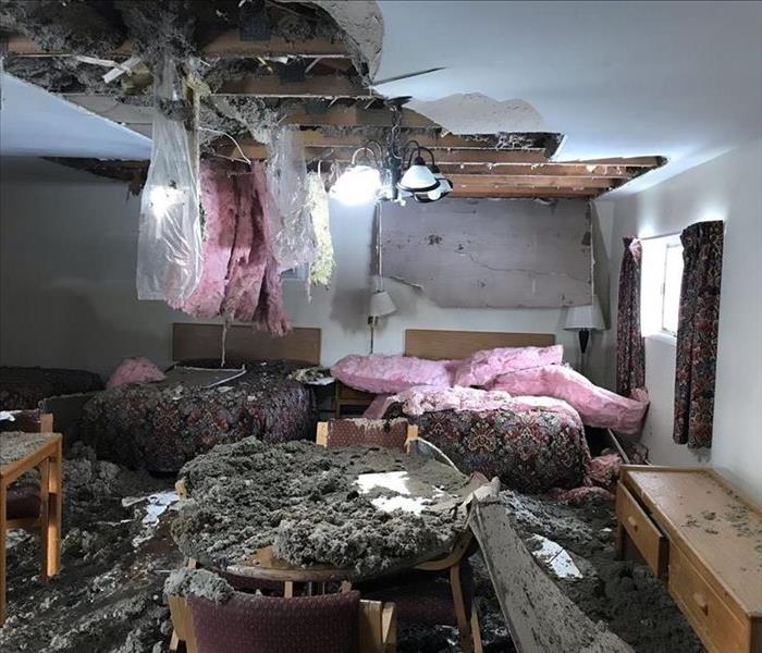 image of motel room with roof caved in and roof and ceiling debris all over both beds and floor