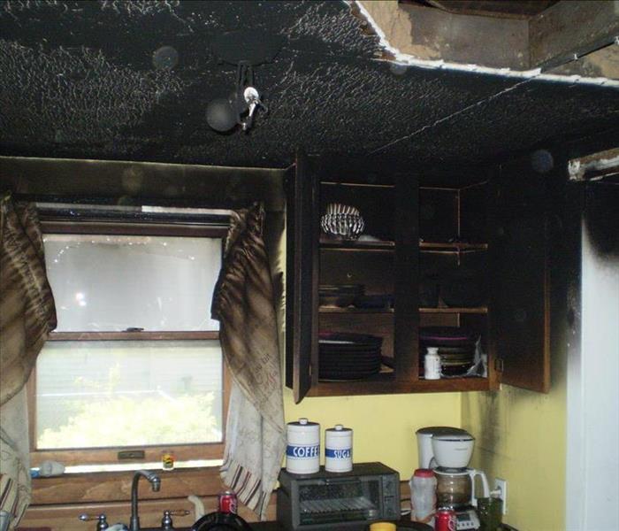 Image of a kitchen with burned cabinets, curtains, ceiling and walls.