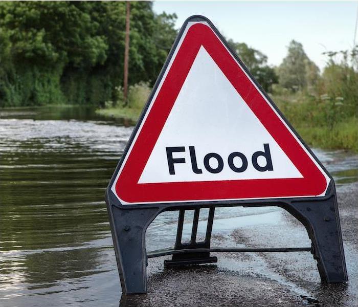 image of a flooded road, trees in background and a Flood sign on small part of road with low water